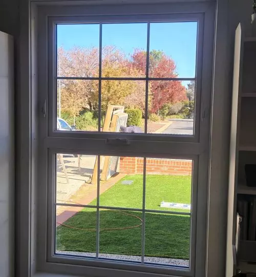 A white UPVC casement window in a room with a grassy yard.